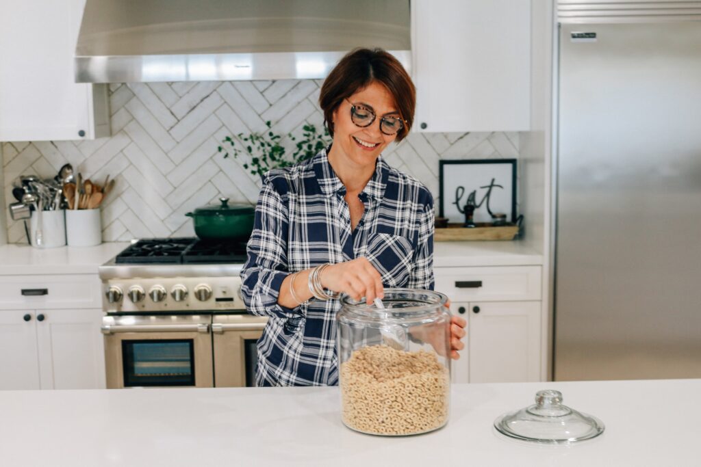 A woman in glasses is stirring something inside of a glass container.