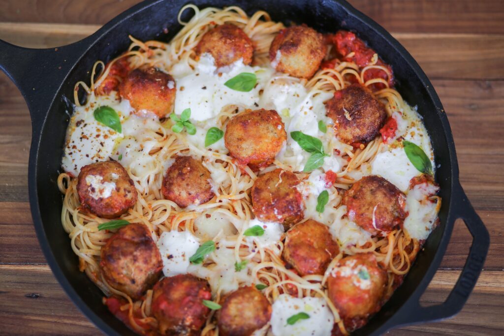 A pan of spaghetti and meatballs with cheese.