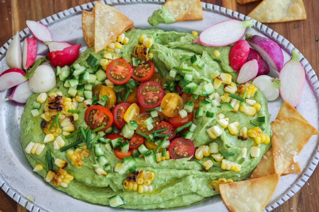 A plate of guacamole with corn, tomatoes and radishes.