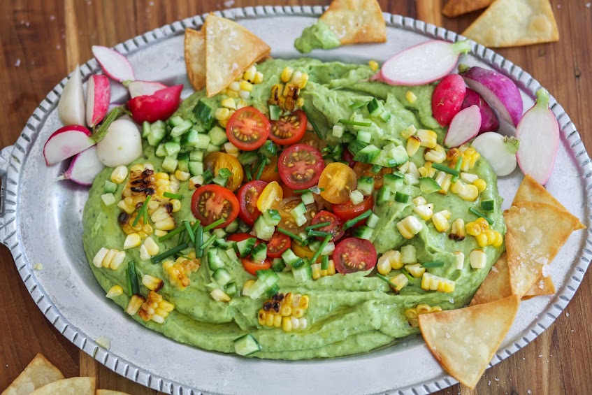 A plate of guacamole with corn and tomatoes.