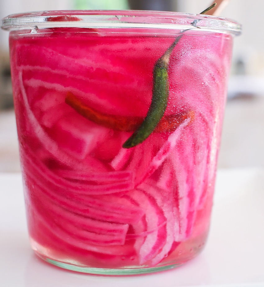 A glass of pickled red onions with a green pepper.