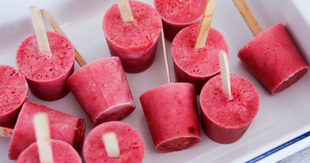 A tray of red fruit juice popsicles with wooden sticks.