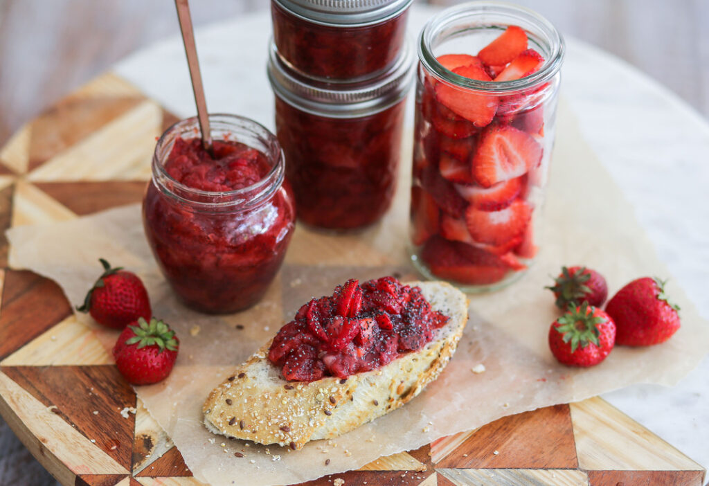 A table topped with jars of strawberry jam next to some strawberries.