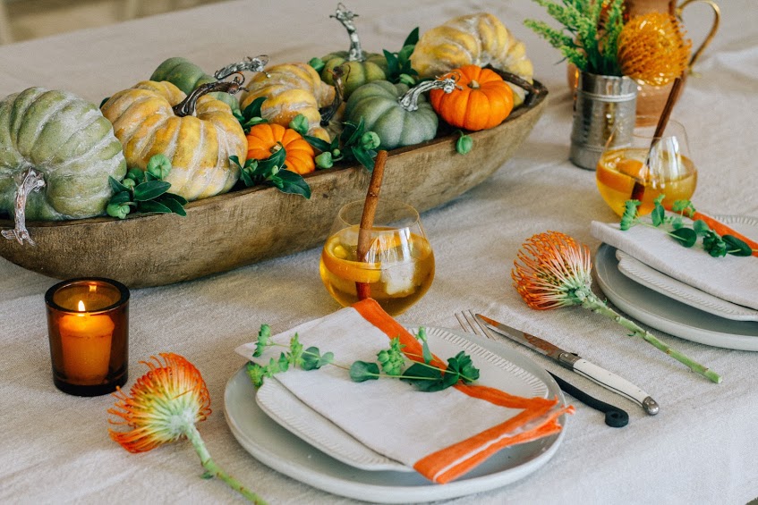 A table set with plates and silverware, pumpkins in a bowl.