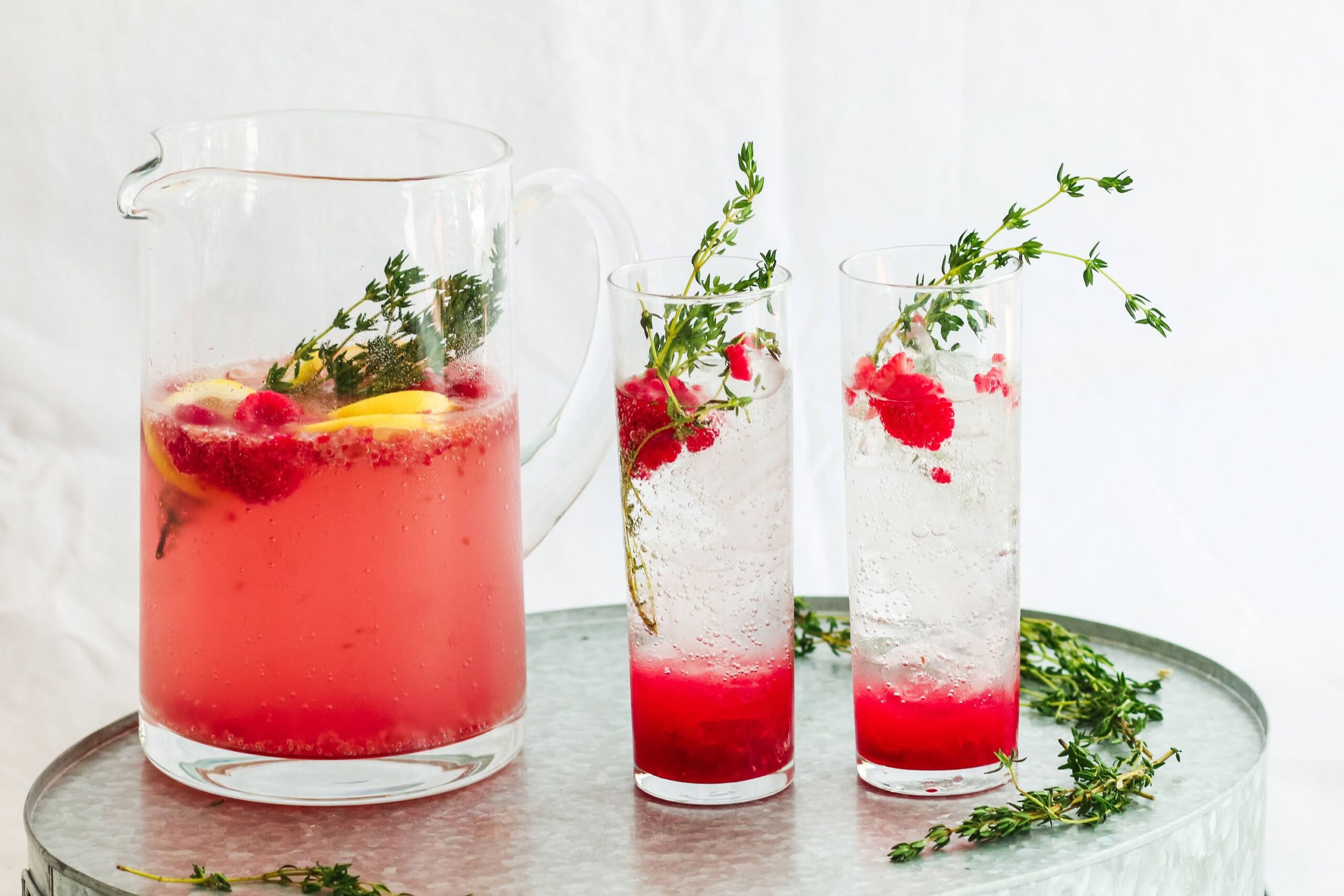 A pitcher and two glasses with water, raspberries and thyme.