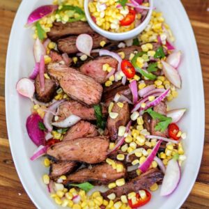 A white plate topped with meat and corn.