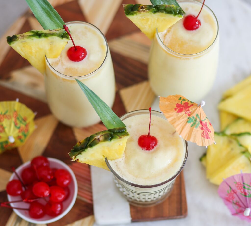 Three glasses of pina colada with a bowl of fruit.
