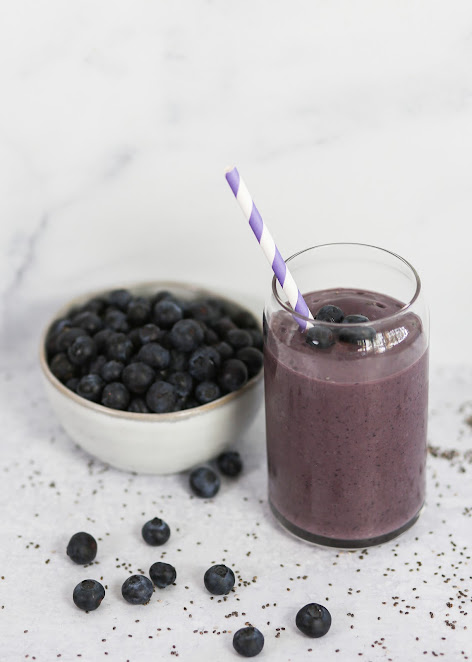 A glass of smoothie next to bowl of blueberries.