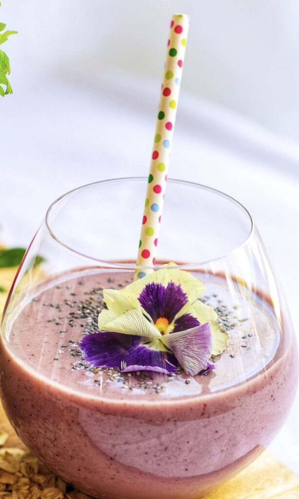 A glass of smoothie with purple flowers in it.