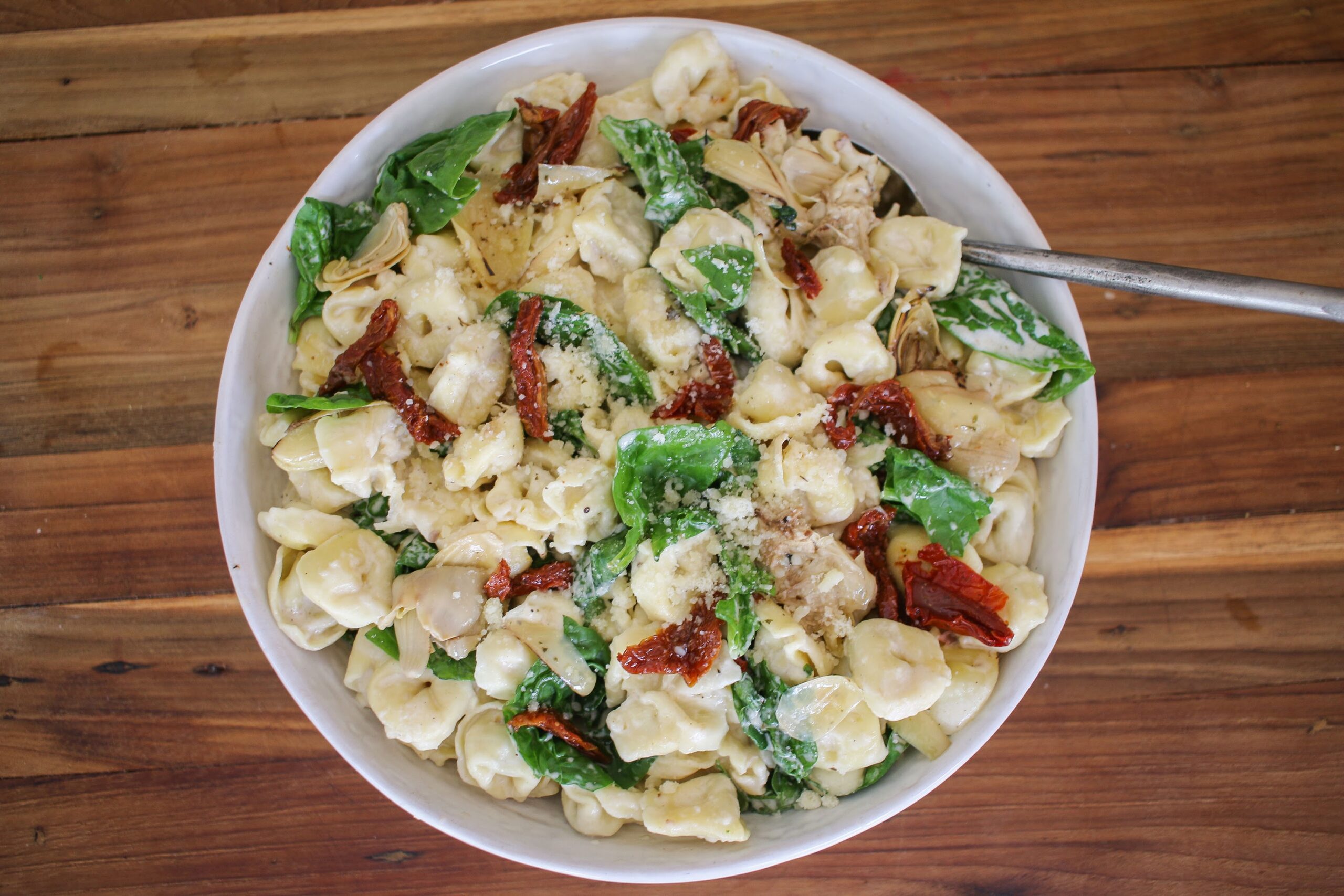 A bowl of pasta salad with bacon and spinach.