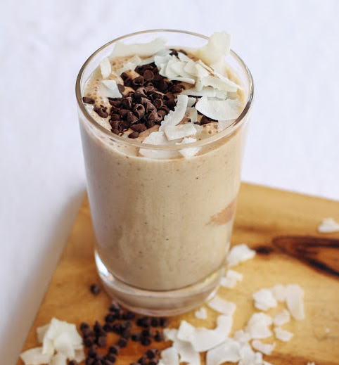 A glass of chocolate shake with coconut flakes on the side.