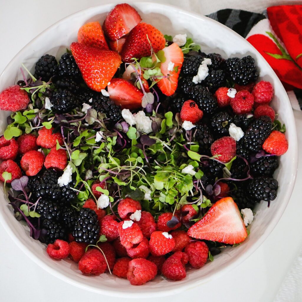 A bowl of mixed berries and greens in a white bowl.