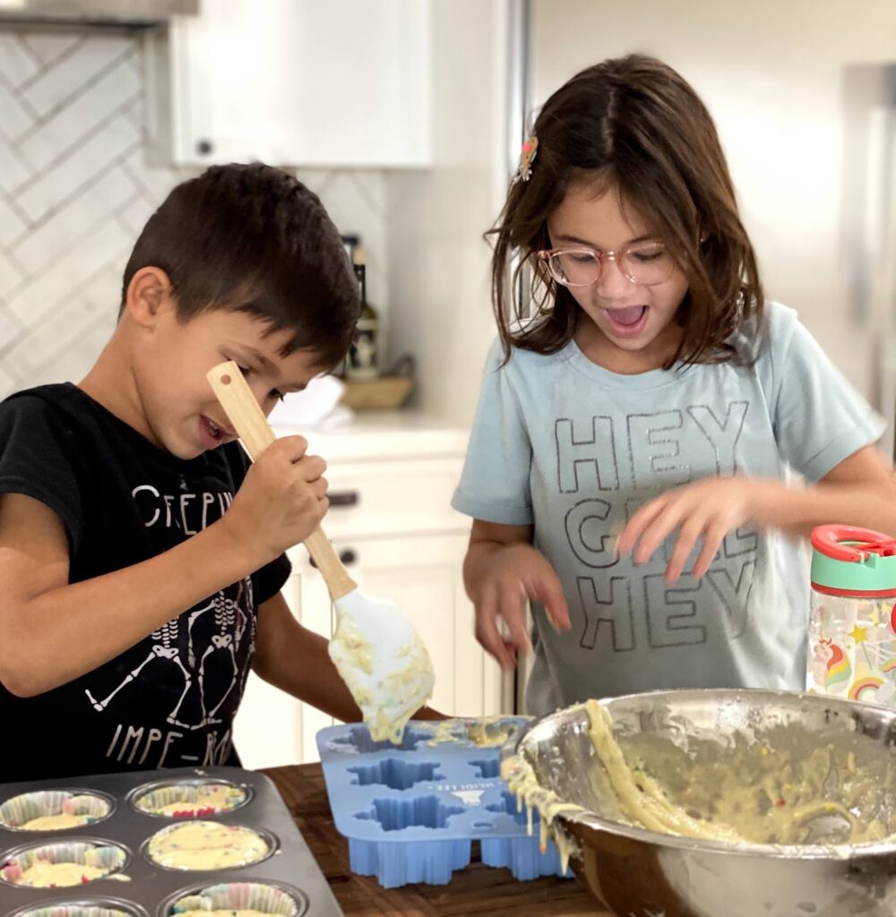Two children are making cupcakes in a kitchen.