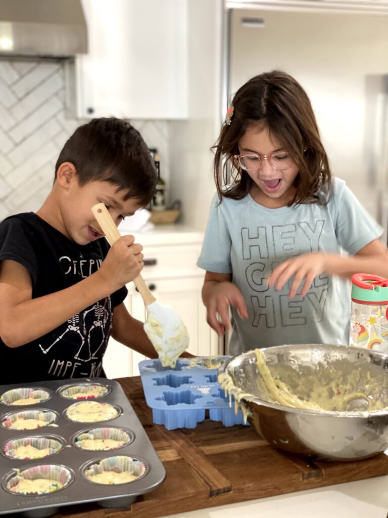 Two children are making cupcakes in a kitchen.