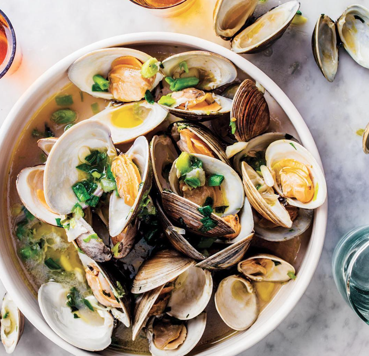 A bowl of clams with broth and herbs.