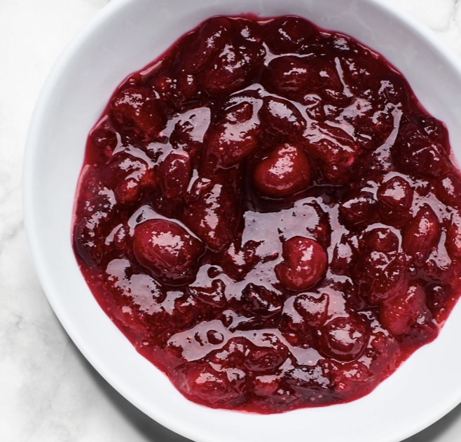 A bowl of cherries in syrup on top of a table.