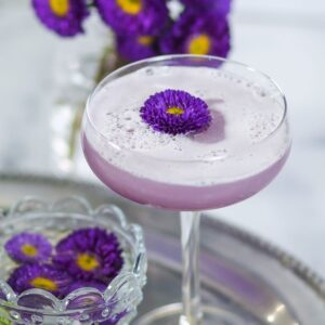 A purple drink in a glass with flowers on the side.
