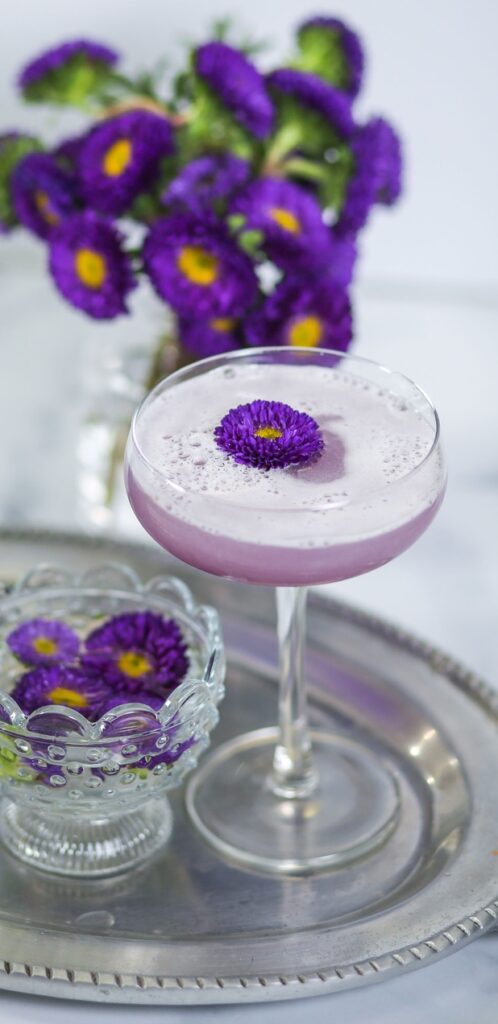 A purple drink in a glass with flowers on the side.