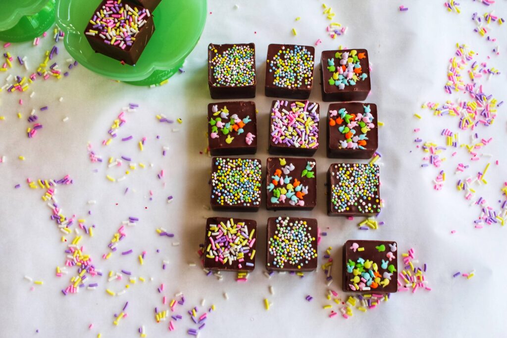 A table topped with lots of chocolate brownies covered in sprinkles.