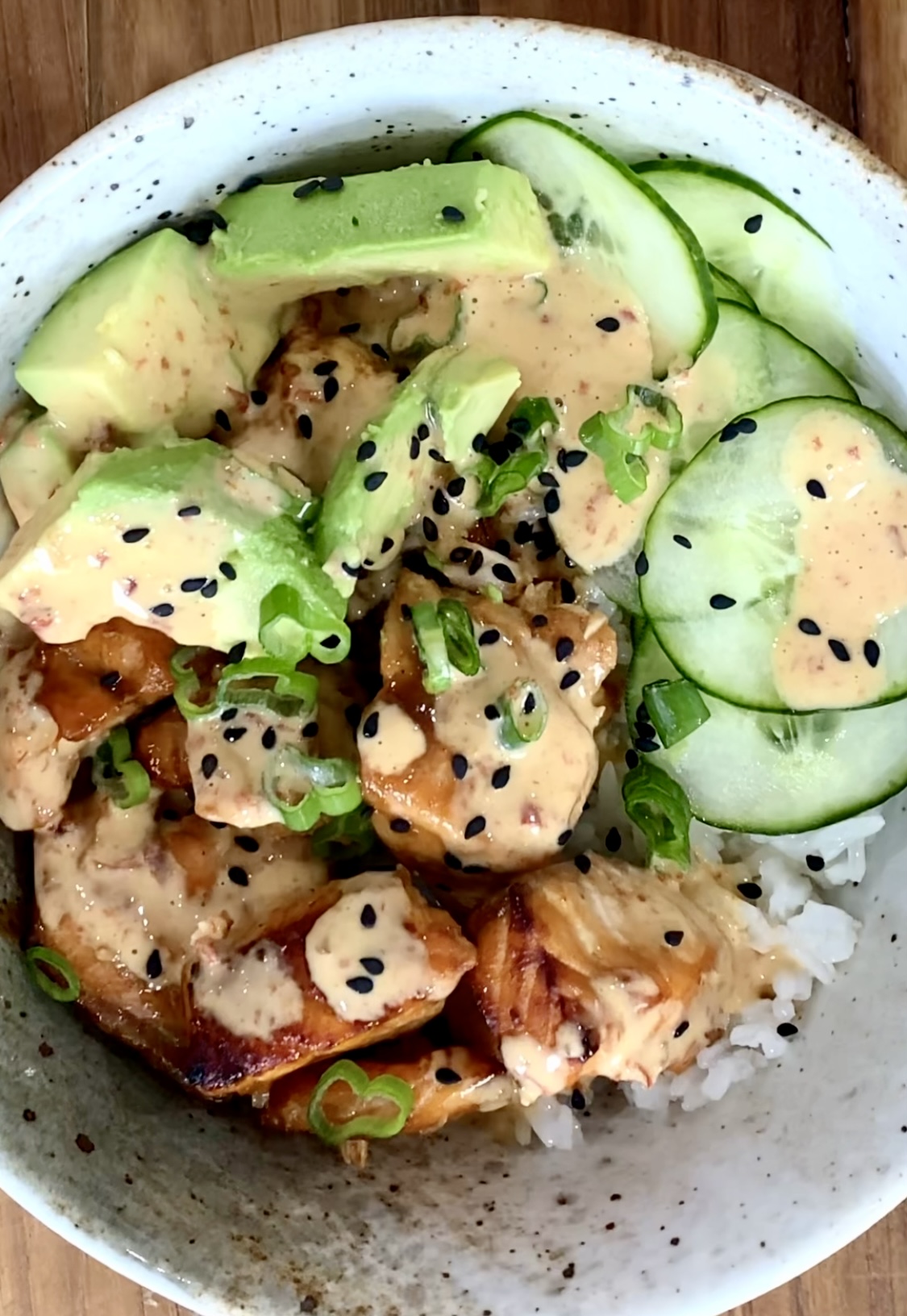 A bowl of food with chicken, cucumbers and sesame seeds.