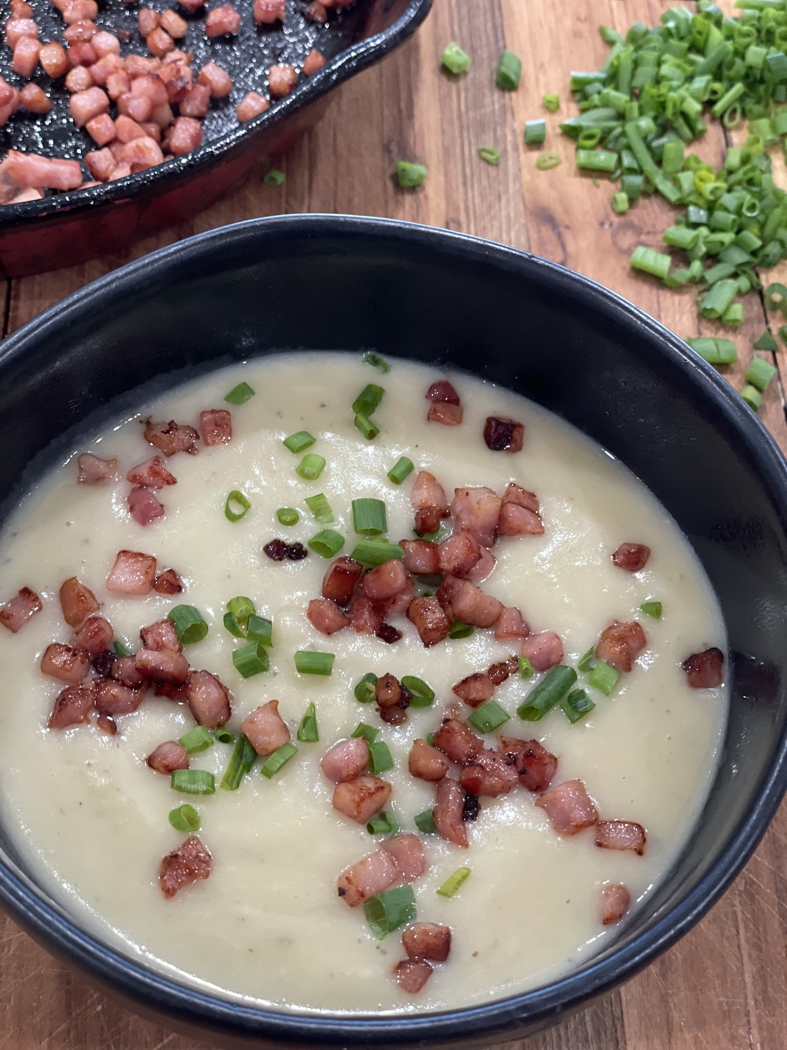 A bowl of potato soup with ham and green onions.