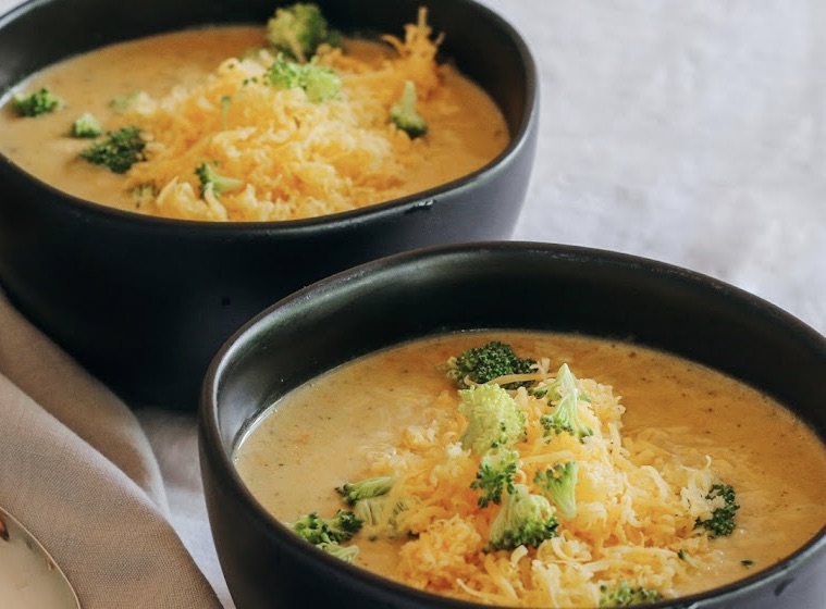 Two bowls of soup with broccoli and cheese.
