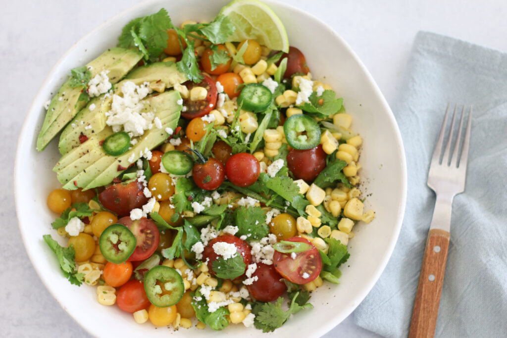 A bowl of salad with tomatoes, corn and feta.