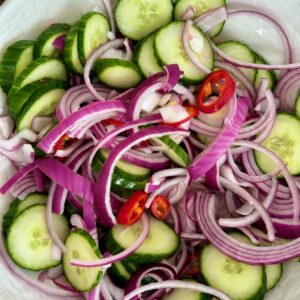 A bowl of salad with cucumbers, onions and peppers.
